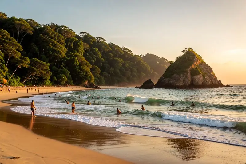 Praia do litoral sudeste com mata atlântica nos morros e surfistas na água ao entardecer