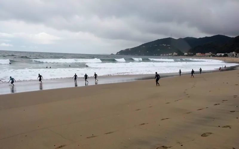Surfistas de roupa de borracha caminhando na areia com ondas quebrando em Tramandaí